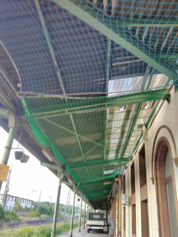 Grünes Schutznetz, das Feld für Feld unter der Stahlkonstruktion einer langen Überdachung eingezogen ist.